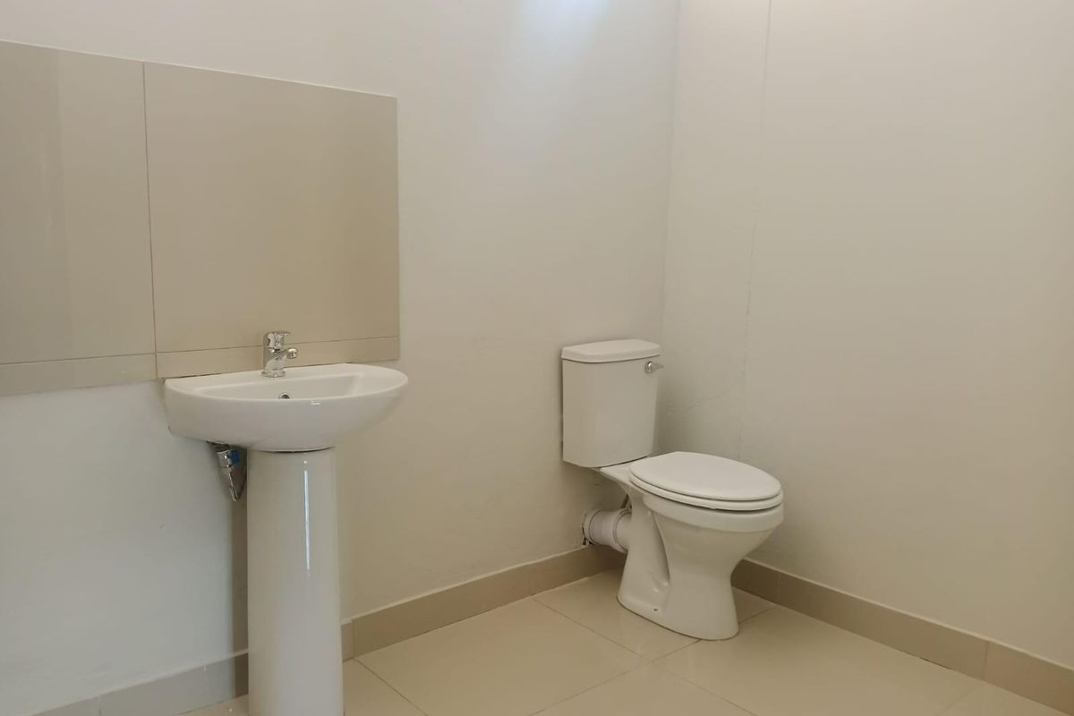 A simple, functional bathroom featuring a white pedestal basin with a wall-mounted mirror and a standard white toilet.