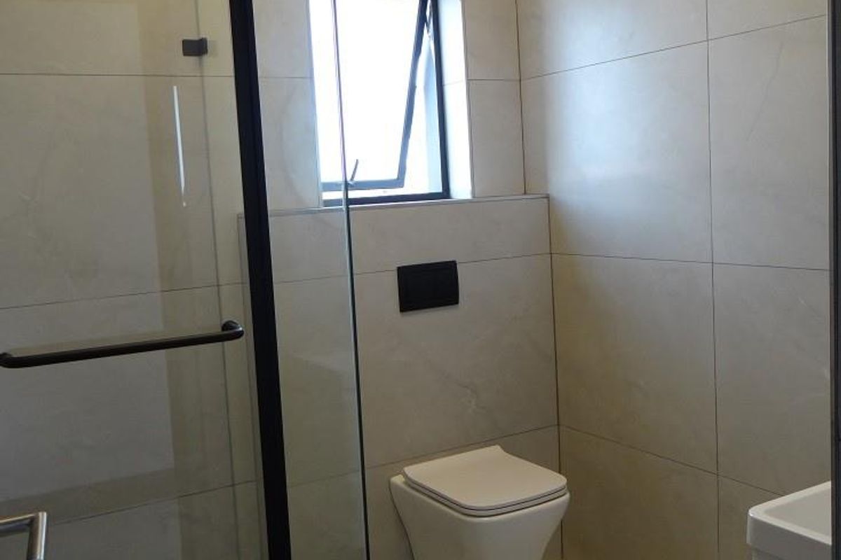 Modern bathroom featuring a frameless glass shower enclosure, wall-mounted toilet, and large-format neutral wall and floor tiles.