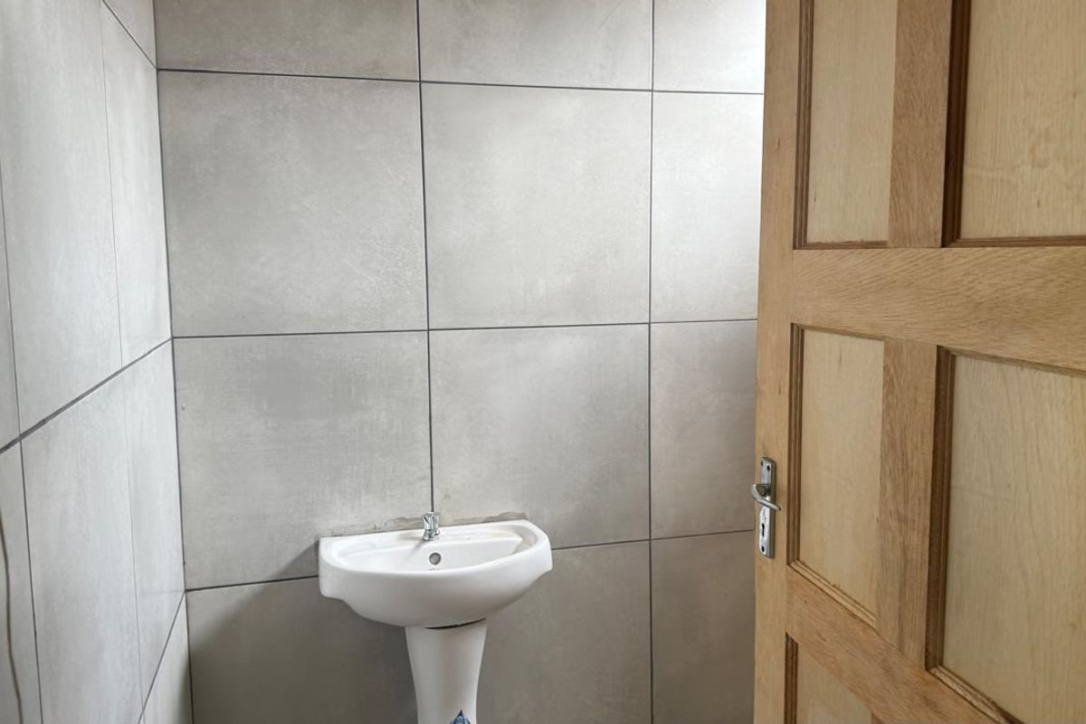 A compact restroom featuring modern grey wall tiles and a white pedestal basin with a wooden door.