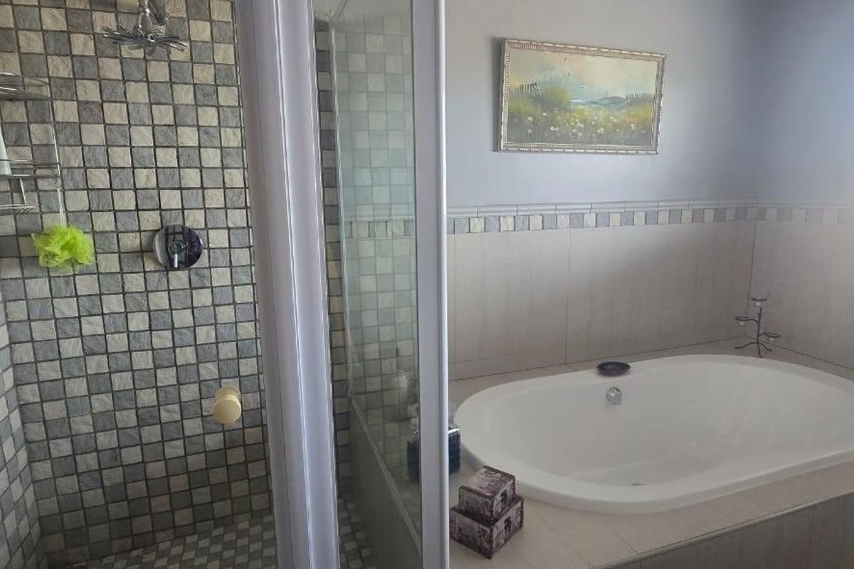 A functional bathroom featuring a built-in bathtub, a separate shower enclosure with mosaic tiling, and a window with fitted blinds.