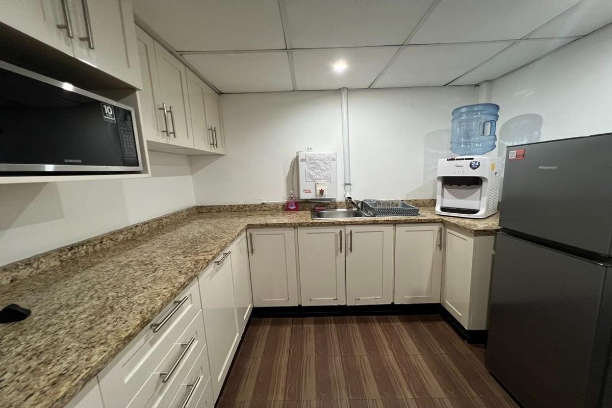 A functional office kitchenette featuring granite countertops, white cabinetry, a stainless steel sink, and a drop ceiling with recessed lighting.