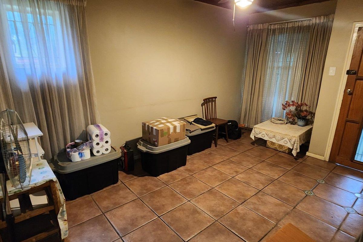 A functional living room space featuring ceramic floor tiles, timber-framed glass panel door, and dual window treatments.