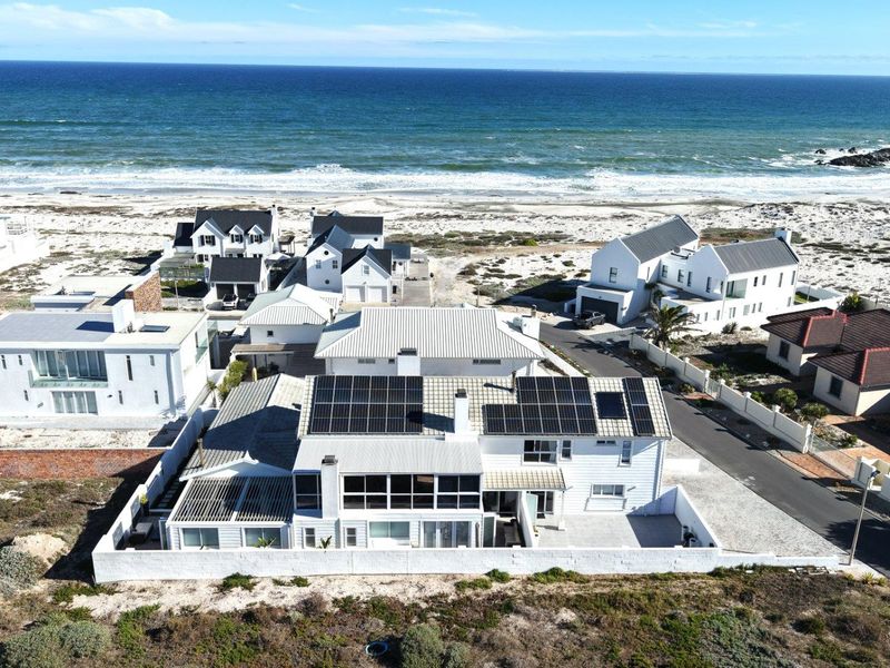 Aerial view of a coastal residential property featuring a white exterior, metal roof, and extensive solar panel installation, situated near the ocean.