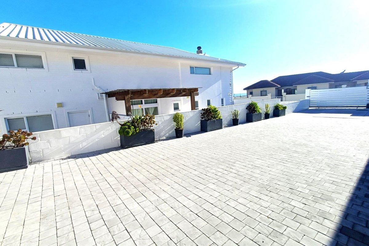 Spacious paved outdoor courtyard area featuring a timber pergola, white boundary walls, and a clean, well-maintained exterior facade.