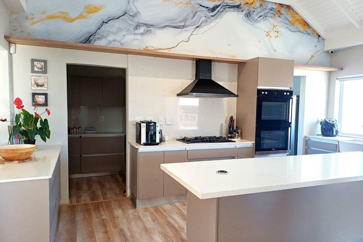 Modern kitchen featuring a central island, built-in double oven, gas hob, extractor fan, and a separate scullery area with neutral cabinetry and stone countertops.
