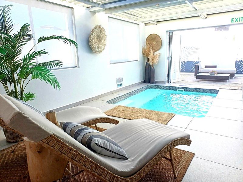 Indoor swimming pool area featuring tiled flooring, large windows, and direct access to an outdoor patio space.