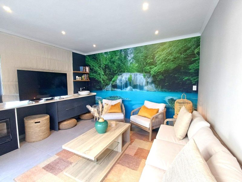A comfortable living room featuring recessed ceiling lighting, a built-in media console with a sink, and a large nature-themed feature wall mural.