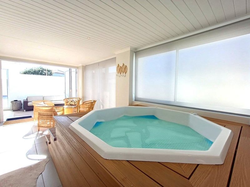 A bright, enclosed patio area featuring a built-in hexagonal spa bath with timber decking, leading out to an open-air outdoor seating space.