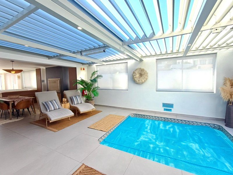 Indoor swimming pool area featuring a retractable louvered roof, tiled flooring, and integrated built-in braai, creating a versatile entertainment space.
