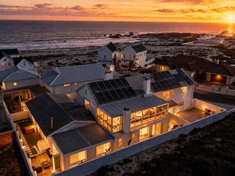 Aerial view of a coastal property at sunset, featuring solar panels, multiple roof pitches, and an enclosed patio area.