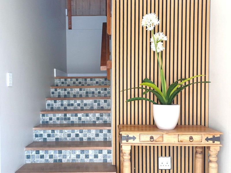 A well-maintained entryway featuring a staircase with decorative mosaic tile risers and a modern vertical timber slat feature wall.