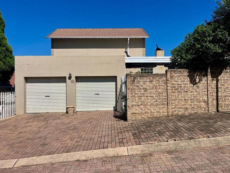 Front exterior view of the property featuring a double garage with roller doors, paved driveway, and a brick boundary wall.