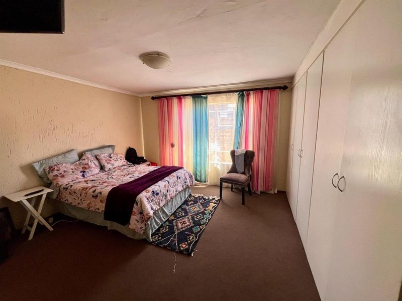 A spacious bedroom featuring built-in wardrobes, carpeted flooring, and a large window with natural light.