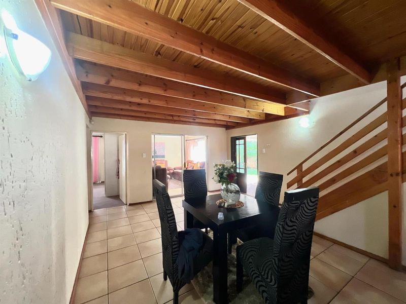Open plan dining area featuring exposed timber beam ceiling, tiled flooring, and a wooden staircase leading to the upper level.