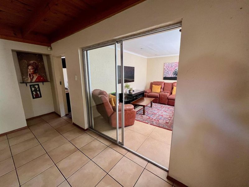 A view from a tiled hallway through a sliding glass door into a living room area with a wooden ceiling feature.
