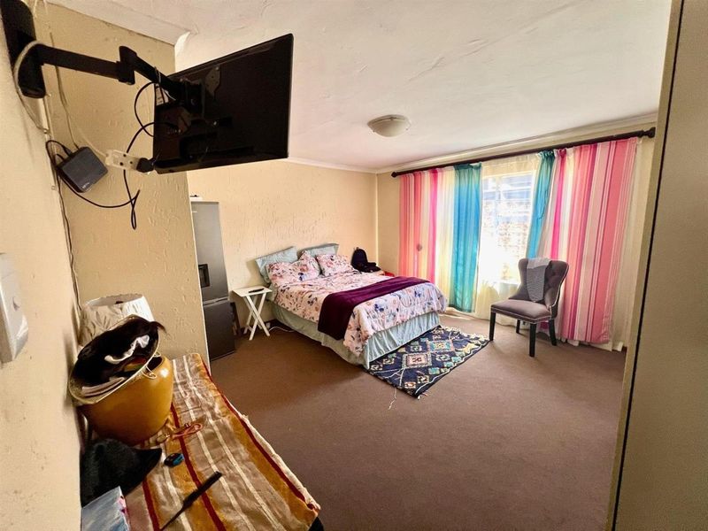 A bedroom featuring carpeted flooring and a window with curtain fixtures, providing a functional sleeping space with potential for cosmetic updates.