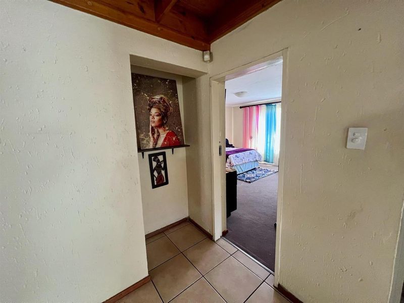 A view from a tiled hallway looking into a bedroom with carpeted flooring and exposed timber ceiling beams.