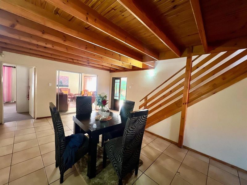 Open plan dining area featuring exposed timber ceiling beams, tiled flooring, and a wooden staircase leading to the upper level.