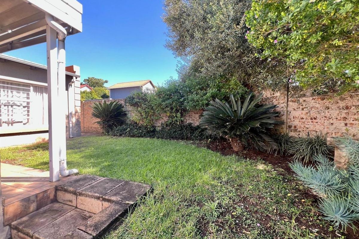 A private rear garden featuring a lawn, established landscaping, and a covered patio area with paved flooring.