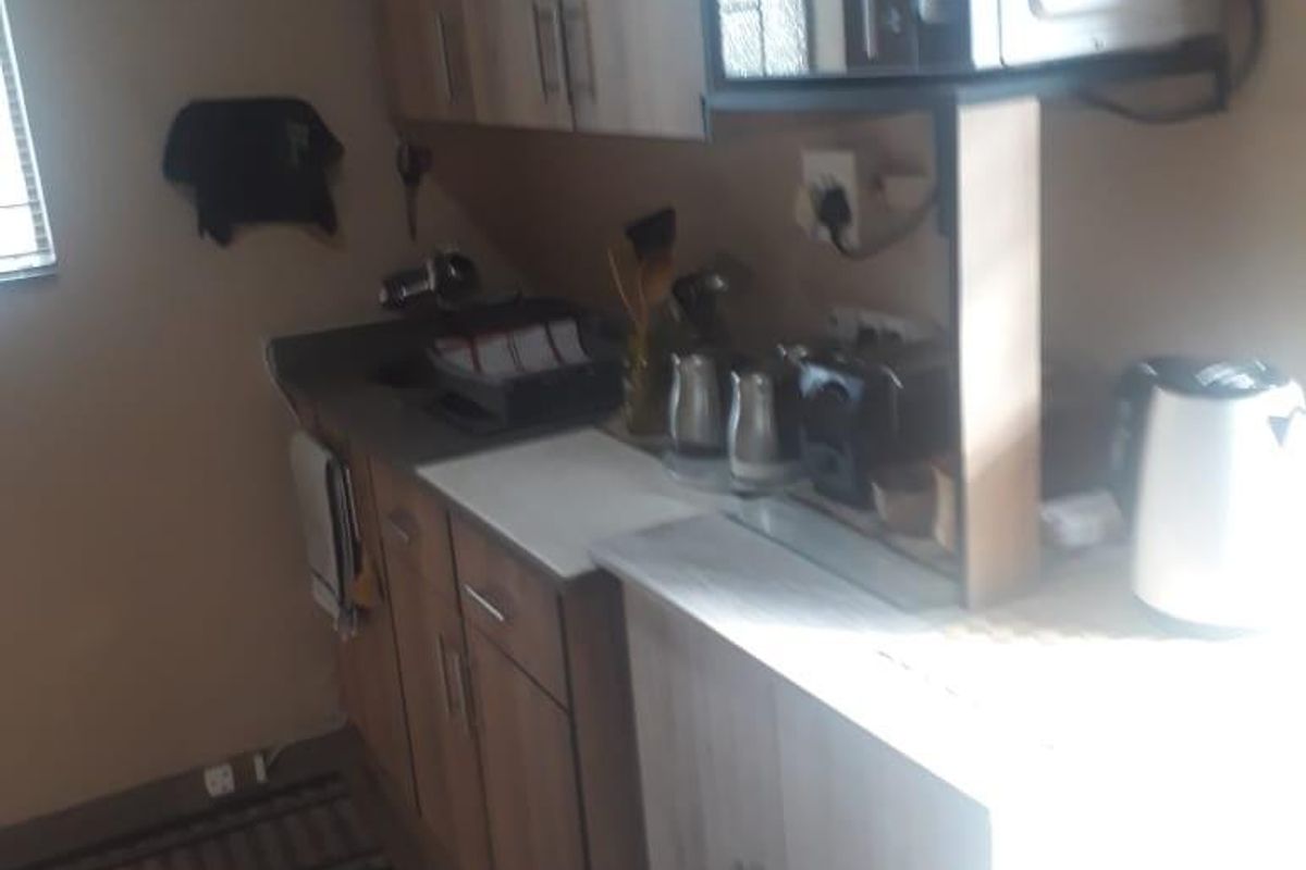 A compact kitchen area featuring wood-look cabinetry, laminate countertops, and a built-in microwave shelf.