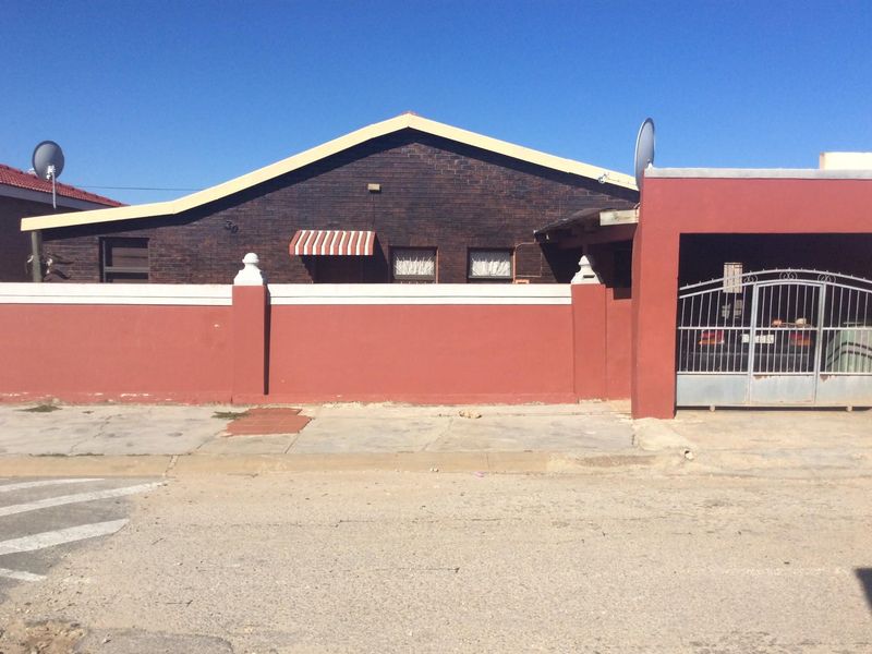 Front exterior view of a brick house featuring a gated carport and a prominent boundary wall.