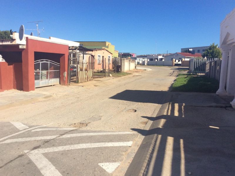 A street view showing the residential road approach with surrounding boundary walls and a metal driveway gate.