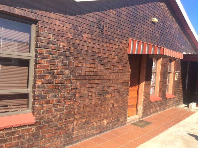 Front exterior view of a face brick house featuring a tiled walkway, striped awning, and aluminium window frames.