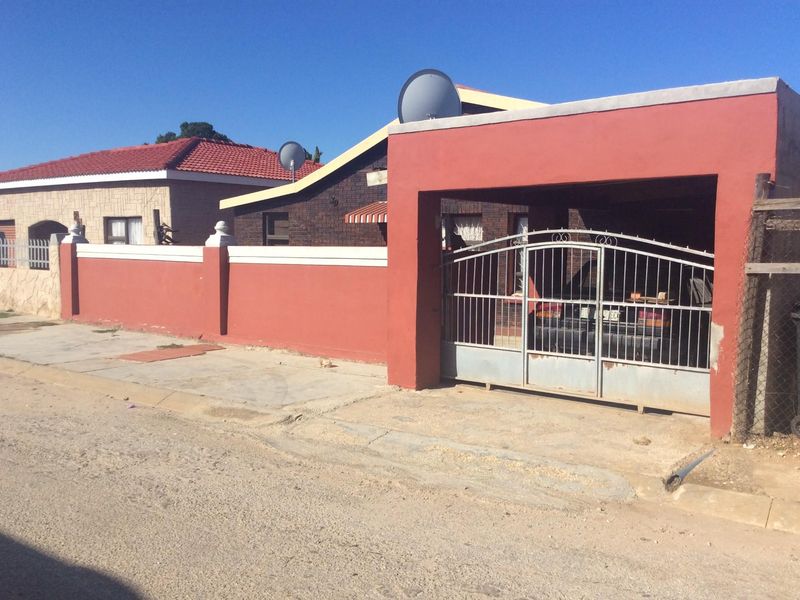 Front exterior view of the property featuring a perimeter wall, metal driveway gate, and a covered carport area.