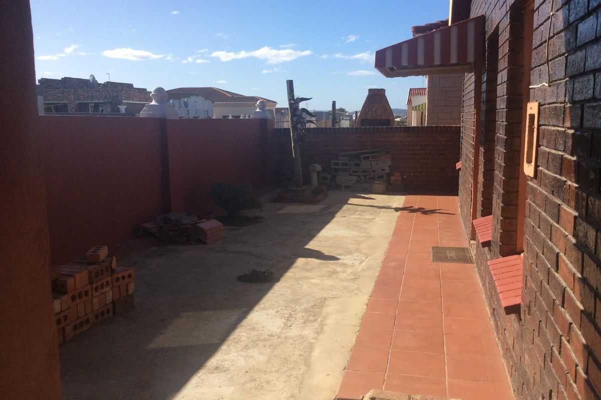 Rear exterior area featuring a brick facade, tiled walkway, and built-in braai, currently requiring landscaping and surface repairs.