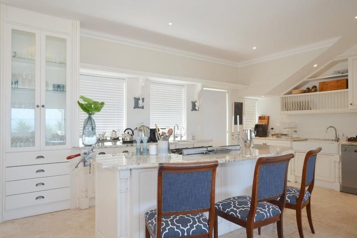 A bright, well-appointed kitchen featuring a central island with stone countertops, custom cabinetry, integrated sink, and classic architectural detailing.
