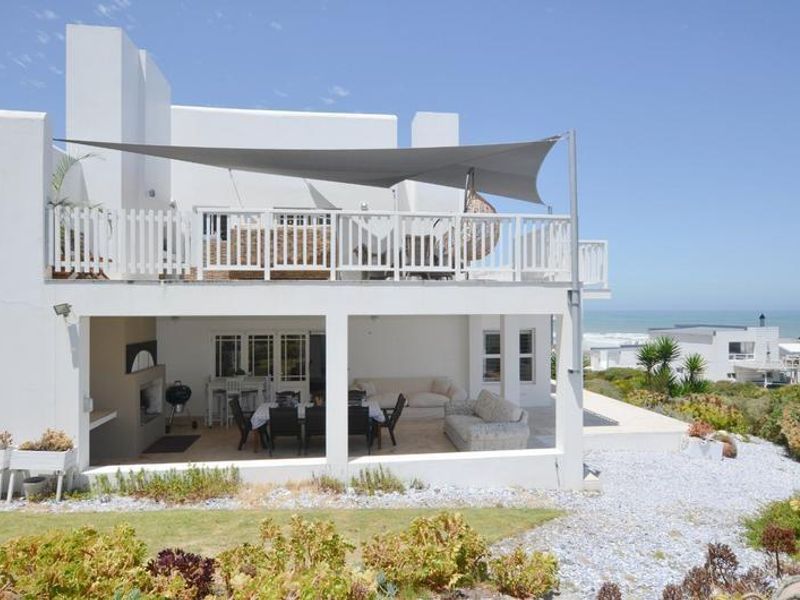 A spacious rear exterior view featuring a covered patio with a built-in fireplace and an upper-level balcony with a shade sail.