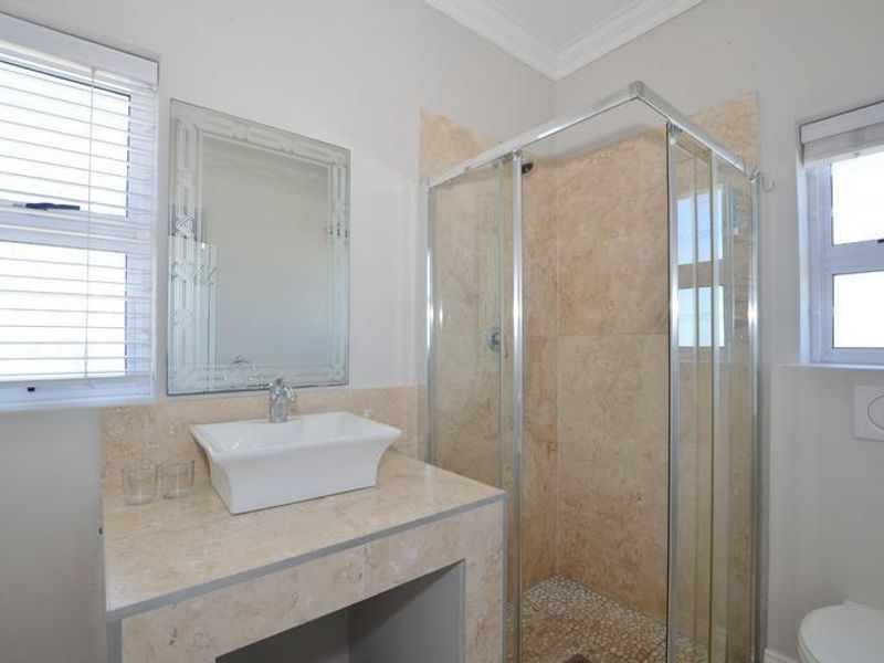 A well-maintained bathroom featuring a stone-tiled vanity with a vessel sink, a glass-enclosed shower with stone wall tiles, and a wall-mounted toilet.