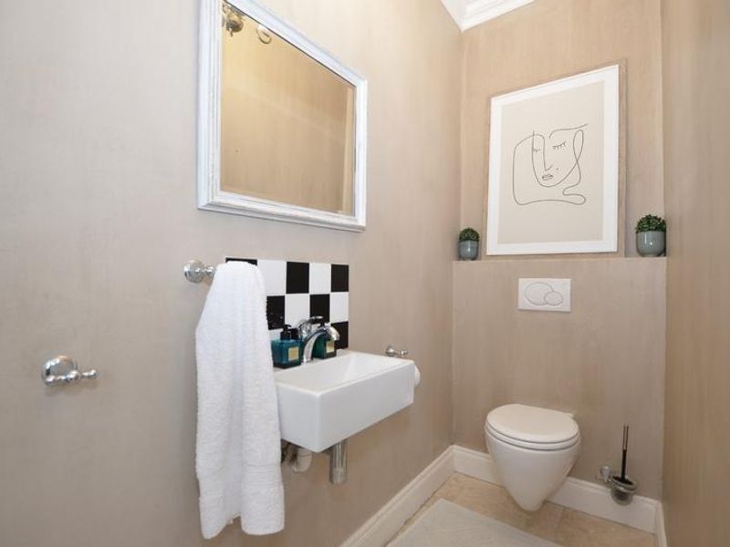A compact guest bathroom featuring a wall-mounted basin with a black and white tiled splashback and a modern wall-hung toilet.