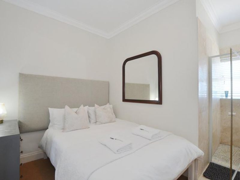 A compact bedroom featuring a built-in headboard and an en-suite bathroom with a glass-enclosed shower and stone-tiled walls.