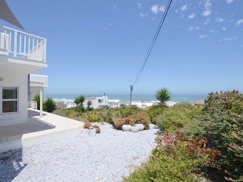 A view of the rear exterior area featuring a paved patio, landscaped garden, and a clear view of the ocean in the distance.