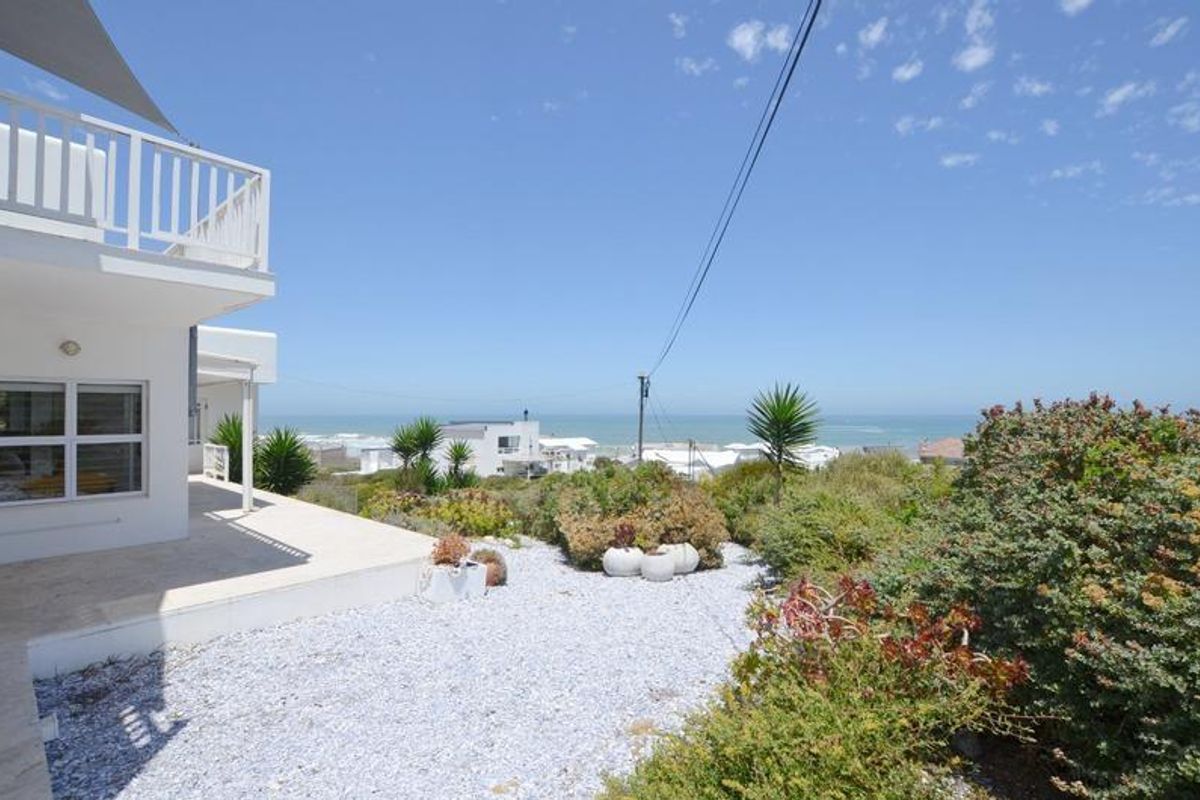 A view of the rear exterior area featuring a paved patio, landscaped garden, and a clear view of the ocean in the distance.