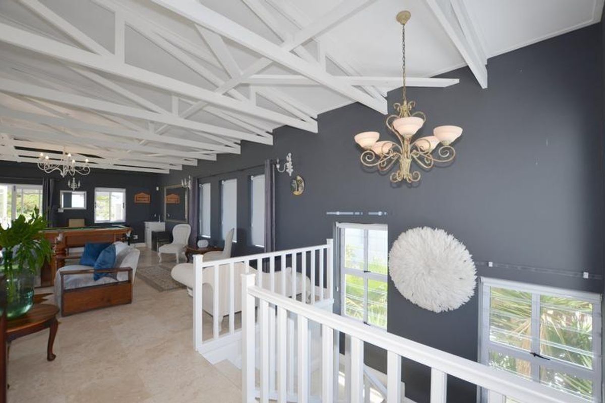 Spacious living area featuring exposed white timber trusses, tiled flooring, and a mezzanine-style layout with a staircase and white balustrade.