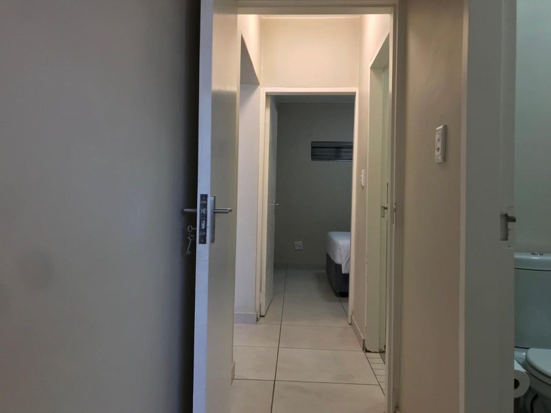 A view through a hallway connecting to a bedroom, featuring tiled flooring and neutral wall finishes.