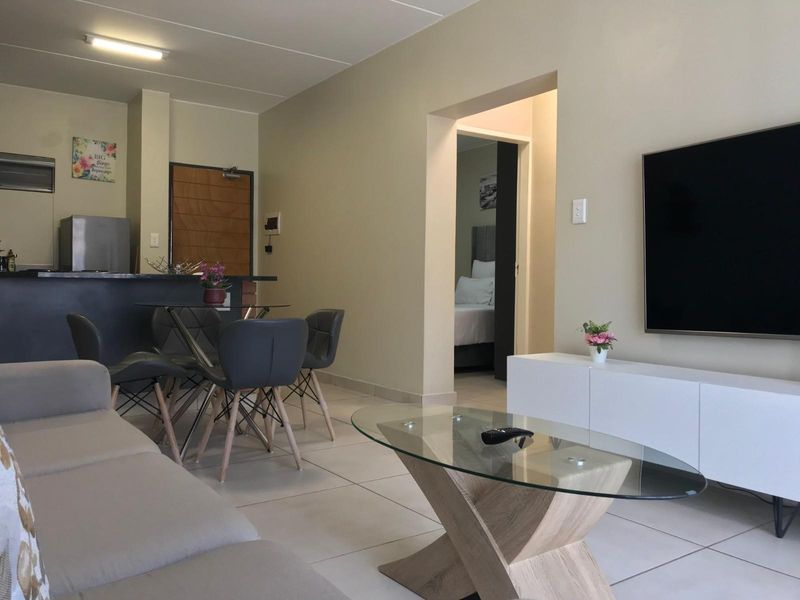 An open-plan living and dining area featuring tiled flooring, a breakfast bar, and direct access to an adjacent bedroom.