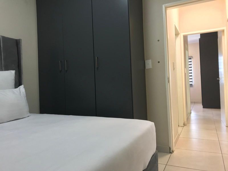 A bedroom featuring built-in dark cabinetry and tiled flooring, with a doorway leading to an adjacent hallway.