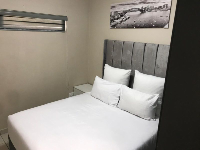 A compact bedroom featuring a neutral color palette, a fitted roller blind, and a built-in power outlet.