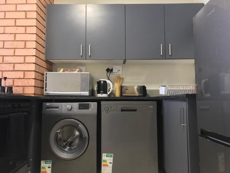 A functional kitchen area featuring dark grey cabinetry, granite countertops, and integrated space for a washing machine and dishwasher.