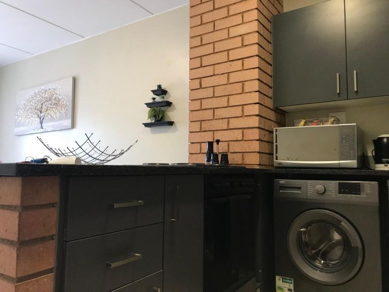 A modern kitchen area featuring dark grey cabinetry, a built-in oven, and a brick feature pillar, providing a contemporary and functional cooking space.