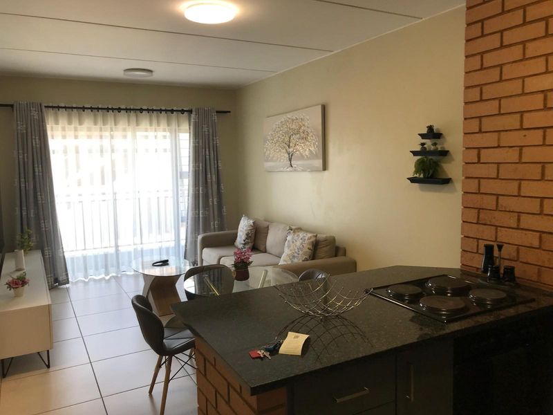 Open-plan living area featuring a kitchen with a built-in hob and breakfast counter, flowing into a lounge space with access to a balcony.