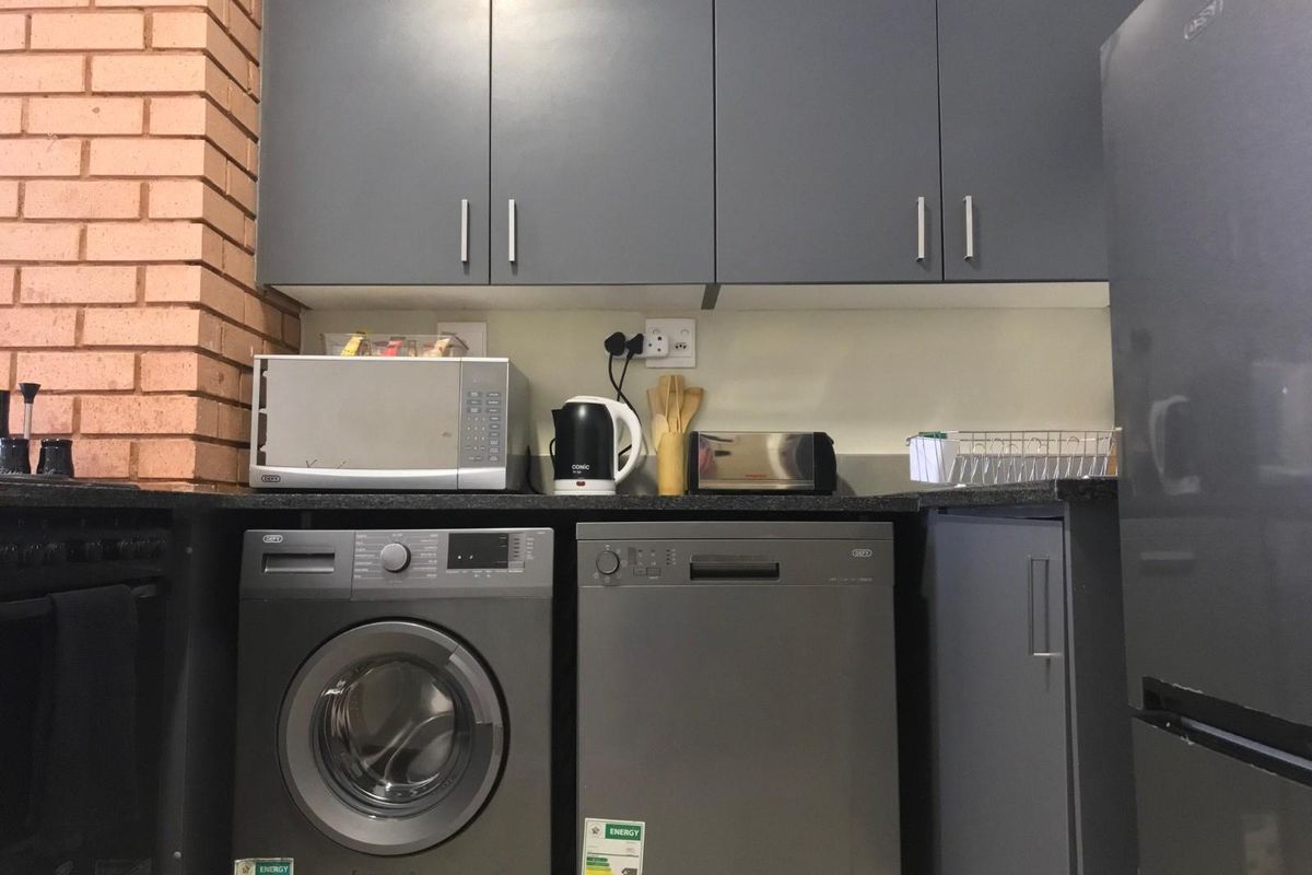 A functional kitchen area featuring dark grey cabinetry, granite countertops, and integrated space for a washing machine and dishwasher.