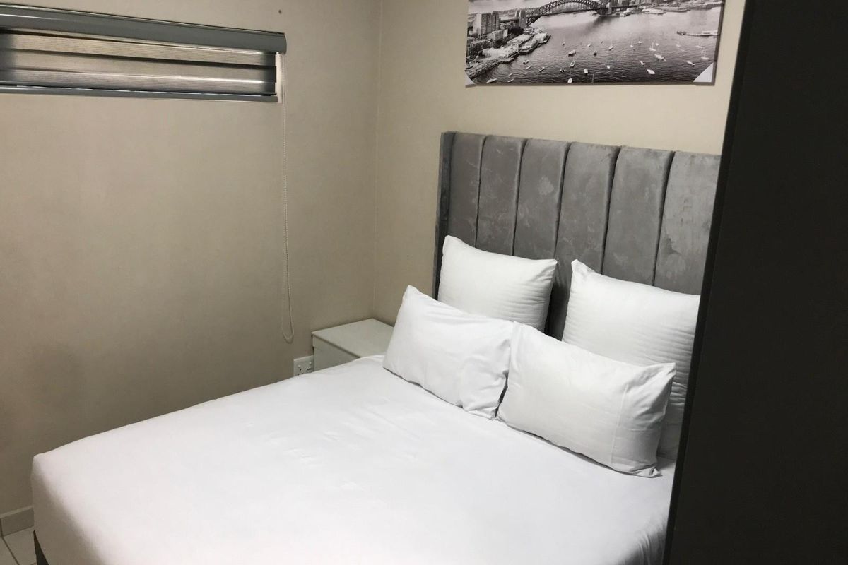 A compact bedroom featuring a neutral color palette, a fitted roller blind, and a built-in power outlet.