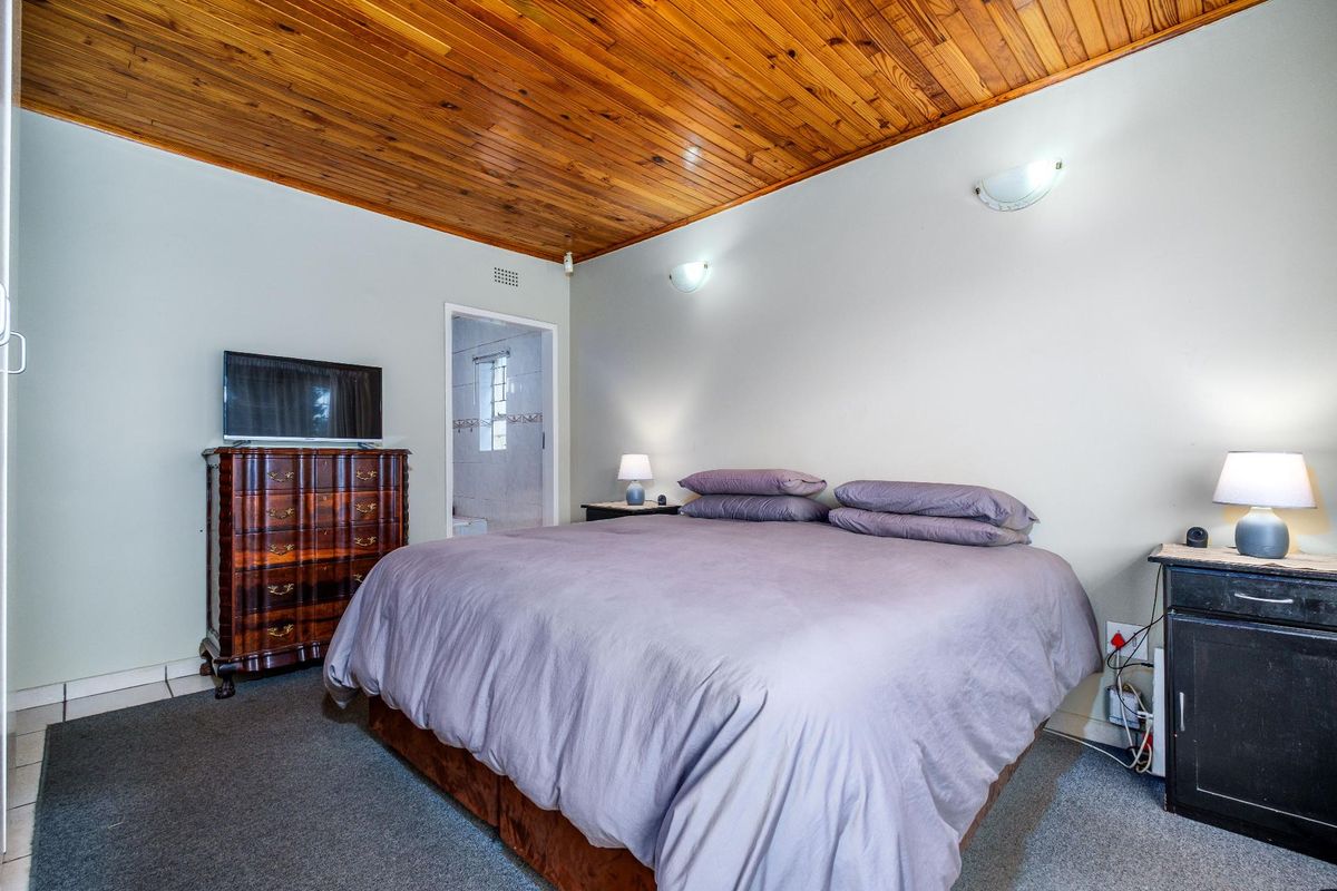 A bedroom featuring a distinctive timber-paneled ceiling, carpeted flooring, and an en-suite bathroom access point.