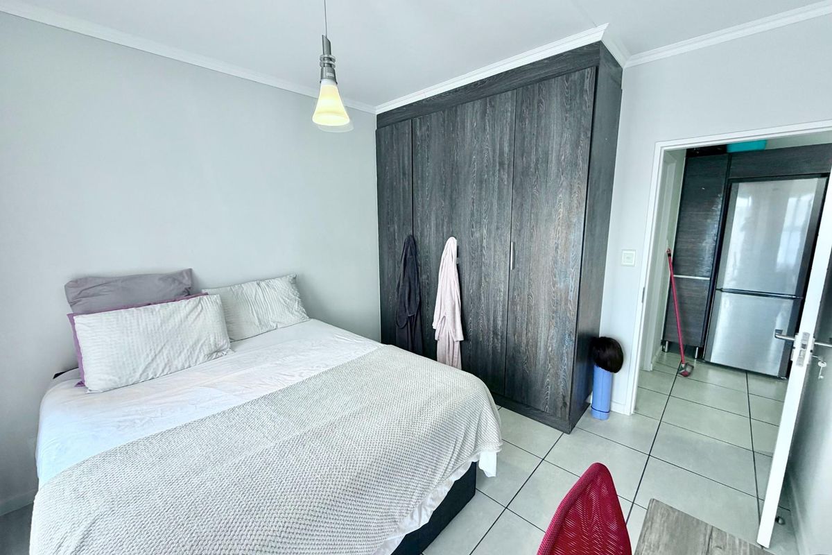 A bedroom featuring tiled flooring, a built-in dark wood wardrobe, and a pendant light fixture, with an adjacent view into a kitchen area.