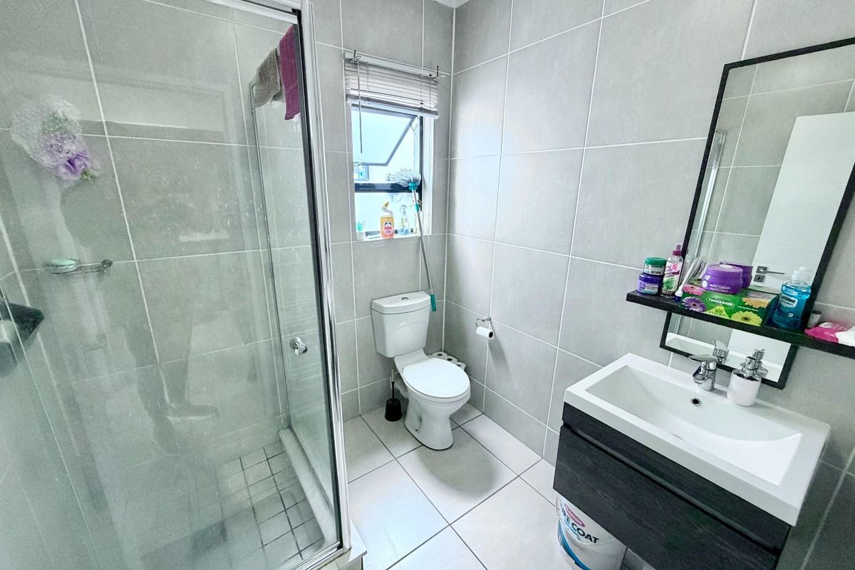 A modern bathroom featuring a glass shower enclosure, vanity cabinet with basin, and neutral ceramic tiling throughout.
