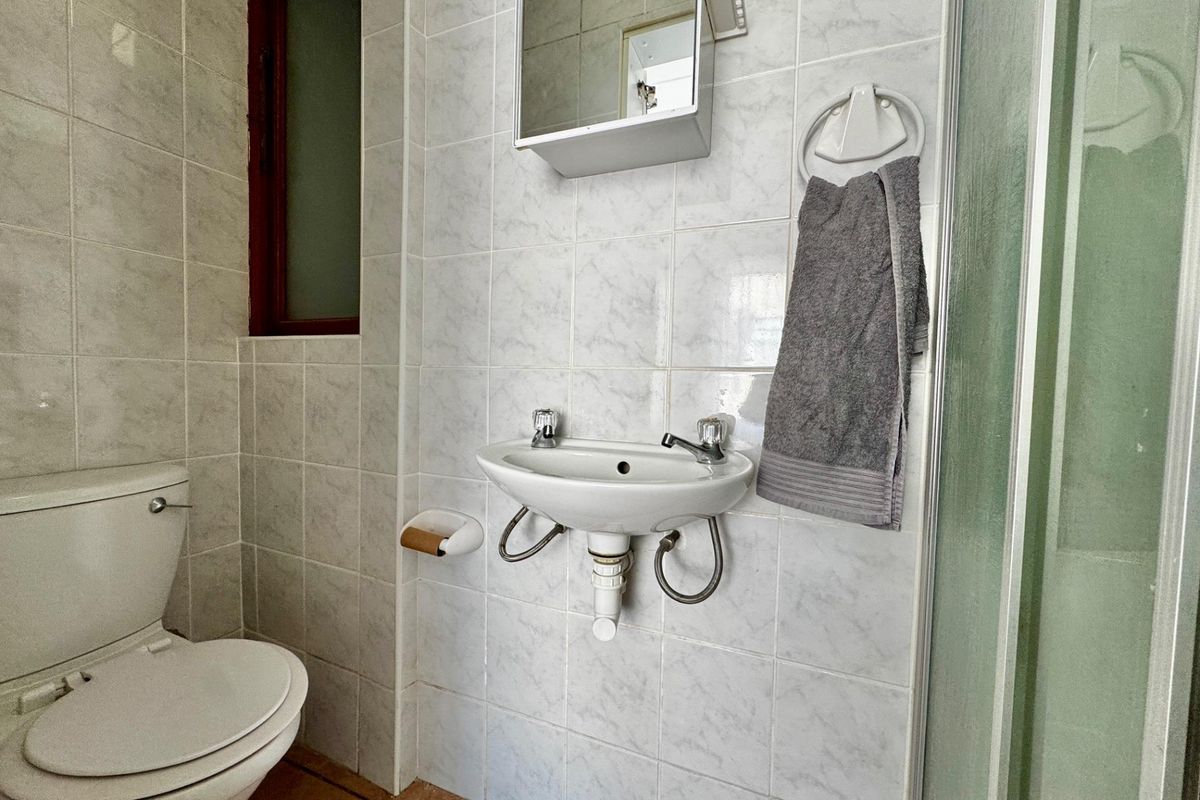 Compact bathroom featuring a wall-mounted basin, toilet, and shower enclosure with tiled walls and flooring.